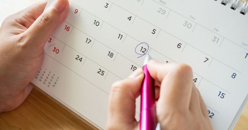 Mani che segnano sul calendario una data di pagamento usando una penna